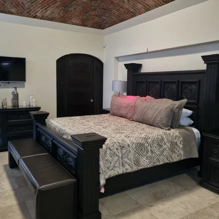 A spacious bedroom at Villa Serena featuring a king-size bed with a four-poster headboard, nightstands with lamps, a television, and a brick vaulted ceiling. - Villa Serena