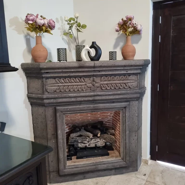 A fireplace at Villa Serena, featuring a stone mantlepiece with intricate carvings, vases with flowers, and a gas-powered flame. - Villa Serena