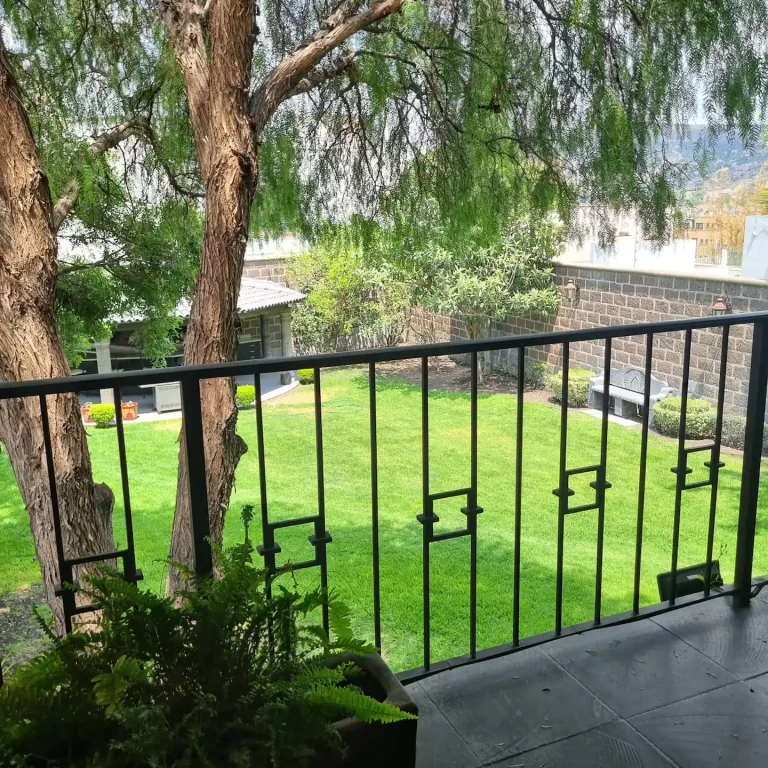 A balcony at Villa Serena overlooking a lush green garden with a gazebo and a stone wall. - Villa Serena