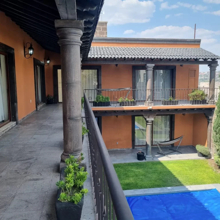 A balcony at Villa Serena overlooking a courtyard with a swimming pool, surrounded by terracotta-colored buildings. - Villa Serena