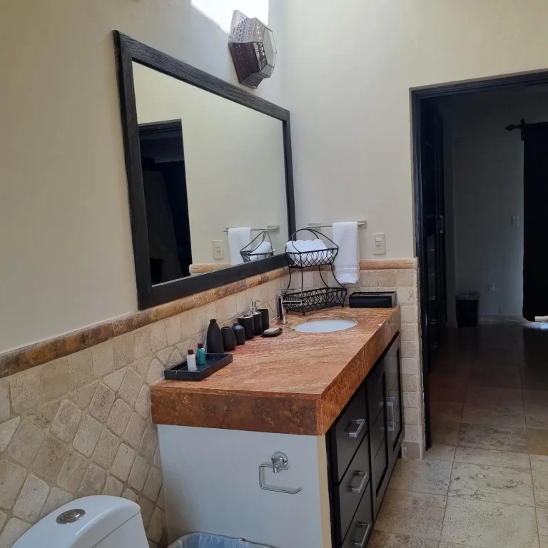 A spacious bathroom at Villa Serena featuring a double sink with a marble countertop, dark cabinets, and a large mirror. - Villa Serena