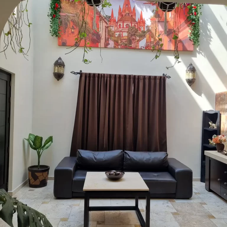 A living room at Villa Serena featuring a leather sofa, a coffee table, a large mural depicting a vibrant cityscape, and hanging plants. - Villa Serena