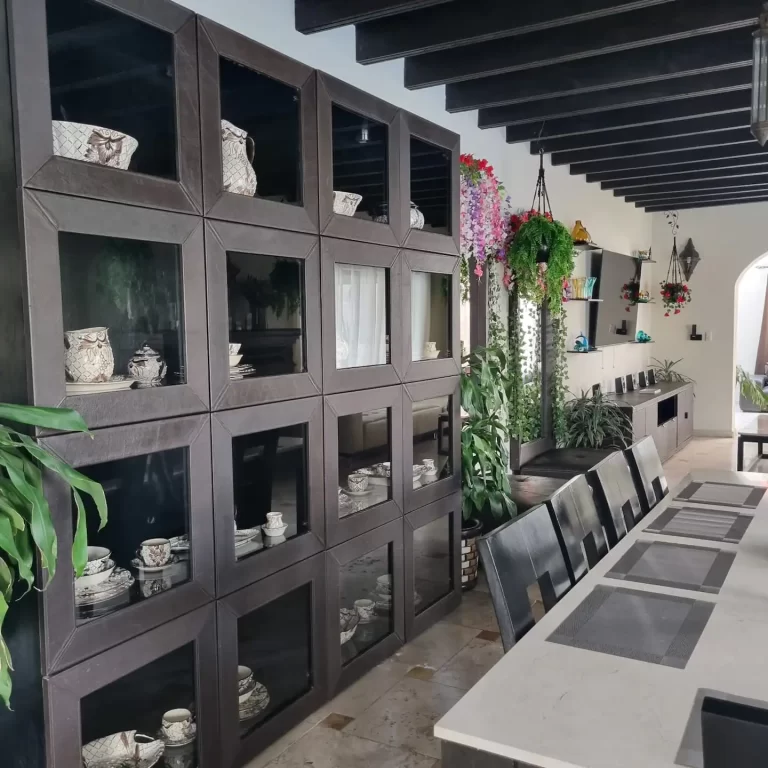 A dining room at Villa Serena featuring a large display cabinet filled with decorative items, a long dining table, and hanging plants. - Villa Serena