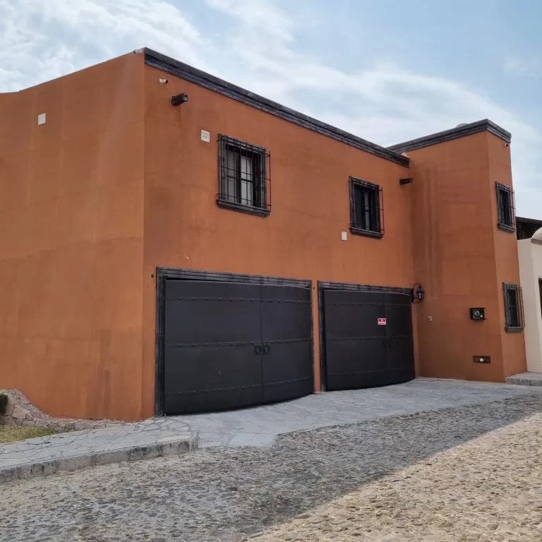 The exterior of Villa Serena, a two-story house with orange stucco walls and black metal garage doors. - Villa Serena