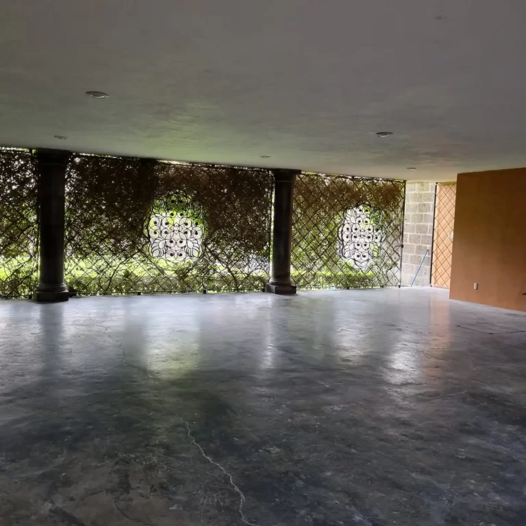 A large empty room with a concrete floor and a wall of metal latticework. - Villa Serena