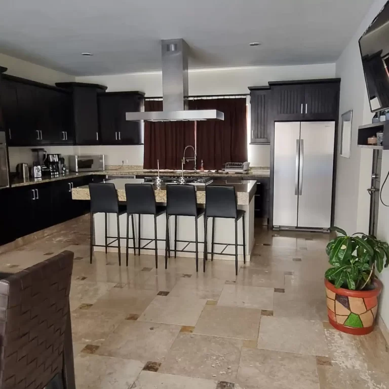 A modern kitchen at Villa Serena featuring black cabinets, stainless steel appliances, a large island with bar stools, and a tiled floor. - Villa Serena